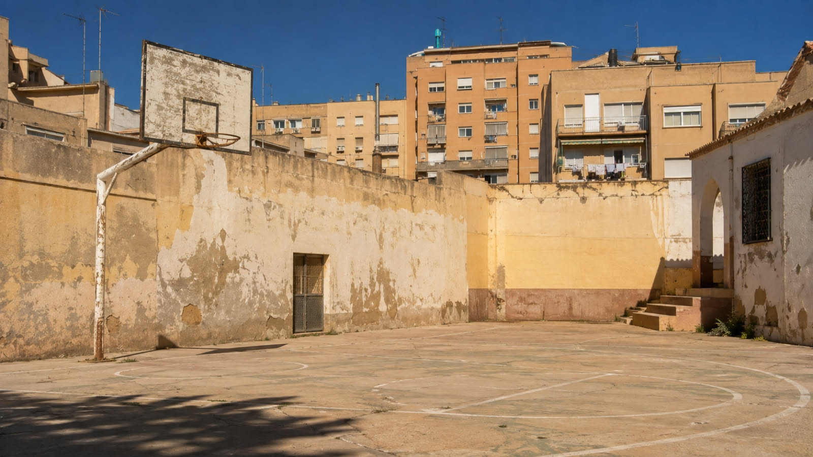 Cortile di un oratorio di periferia con canestro e muro scrostato